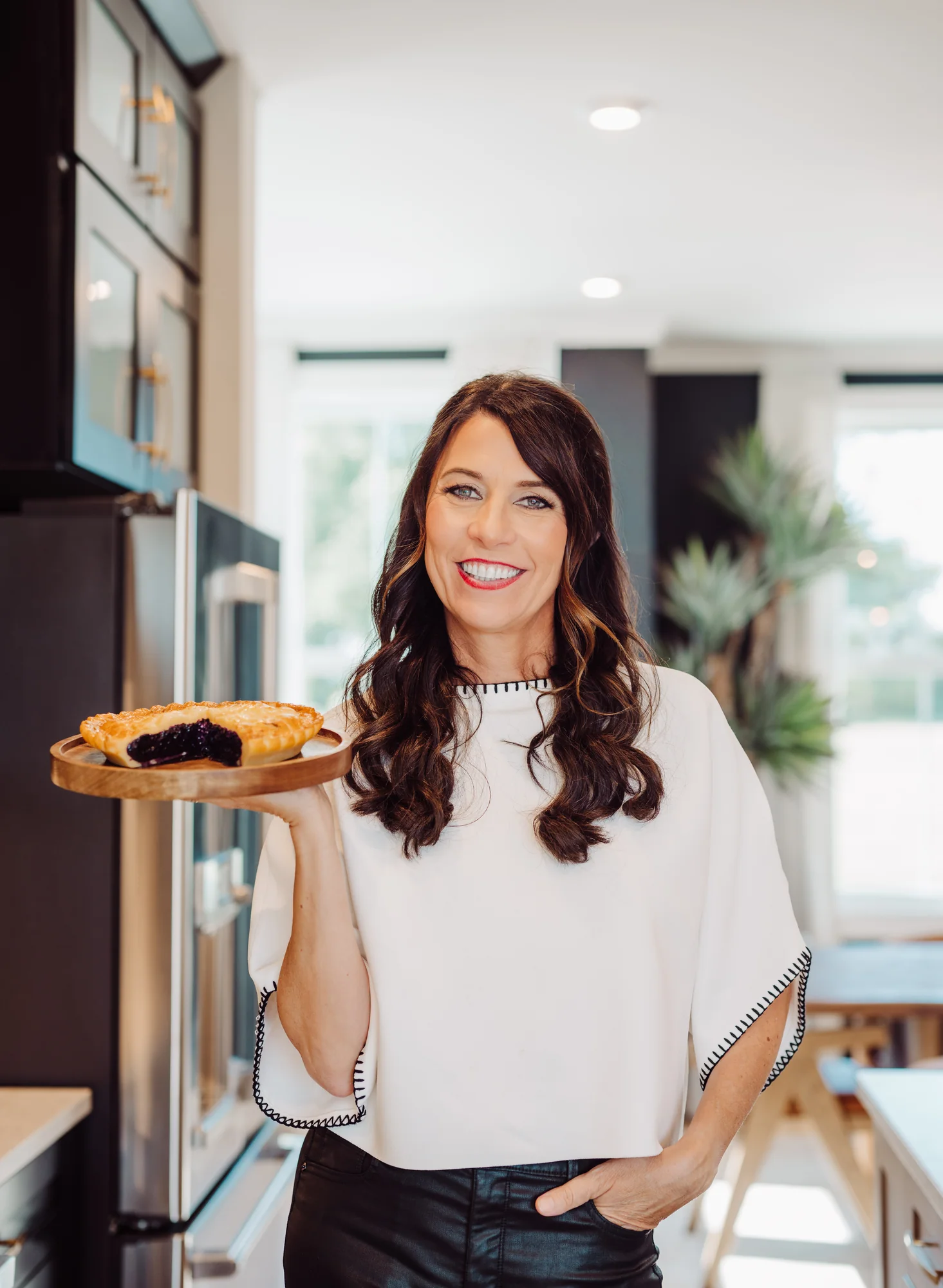 Monika smiling and holding a pie in a kitchen